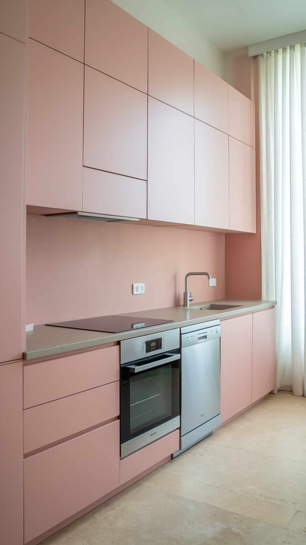 Minimalist blush pink kitchen cabinets with integrated appliances.