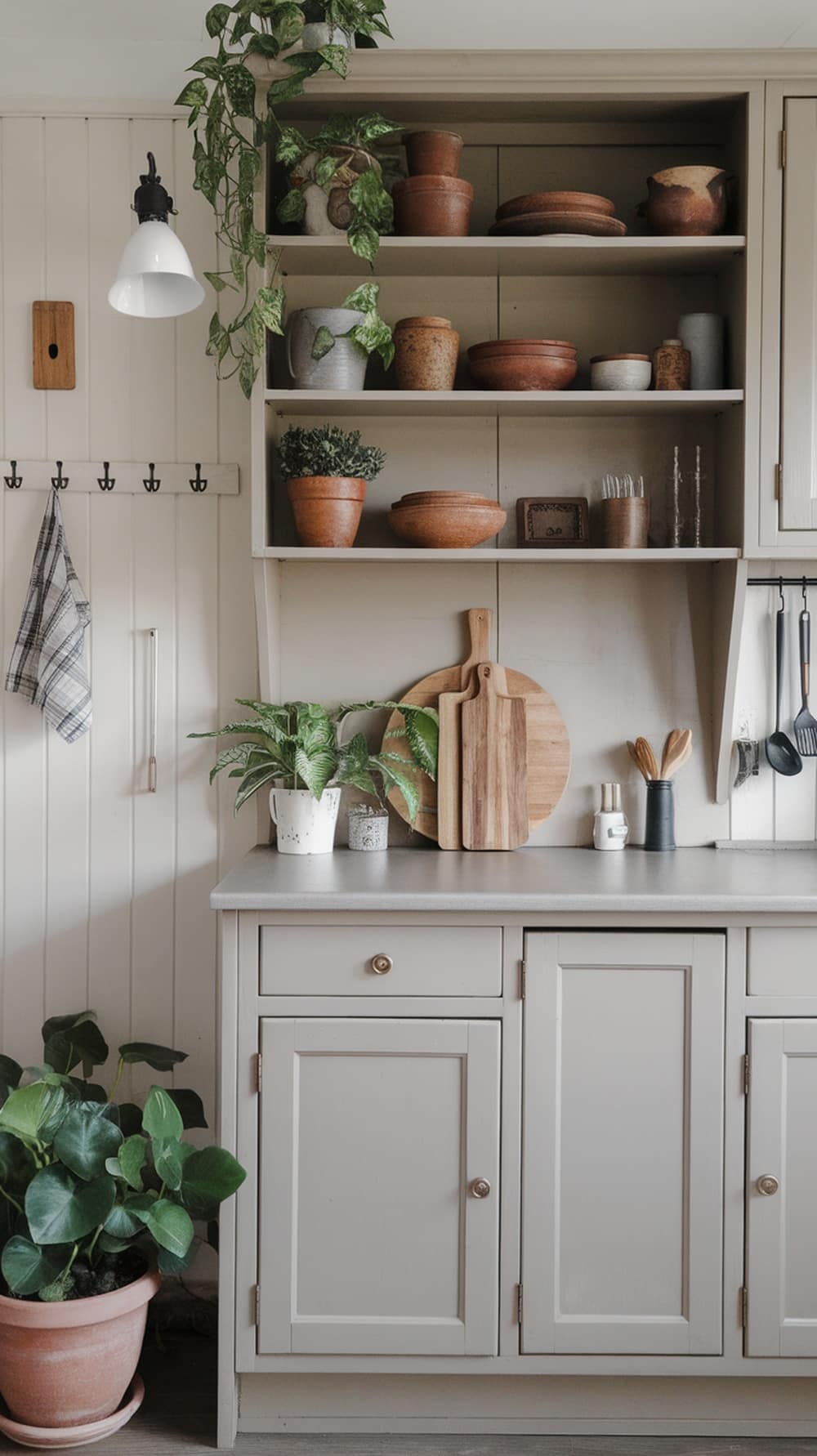 A kitchen featuring greige cabinets and open shelving with plants and pottery.