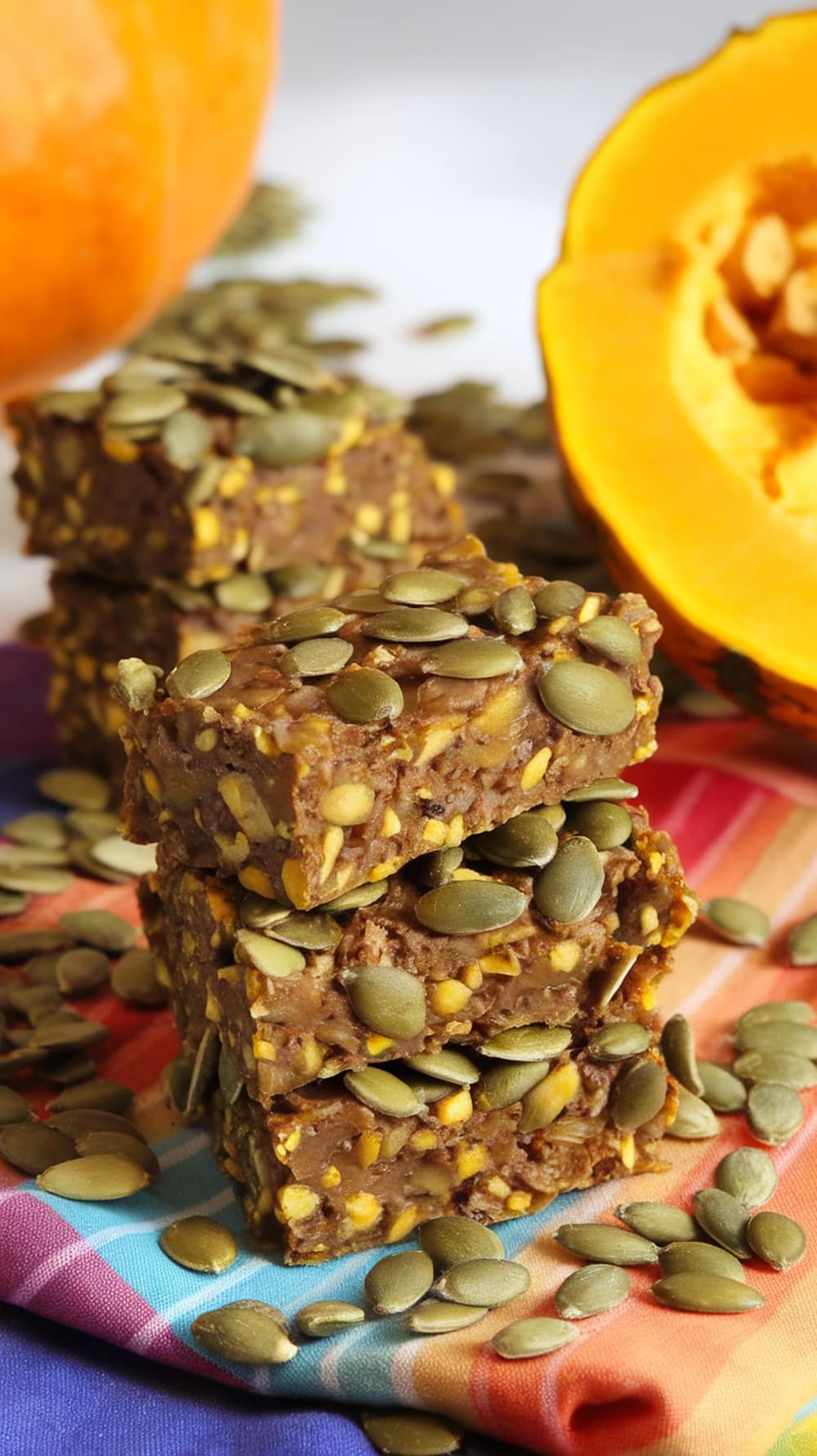 Homemade pumpkin seed energy bars stacked with pumpkin and seeds around them