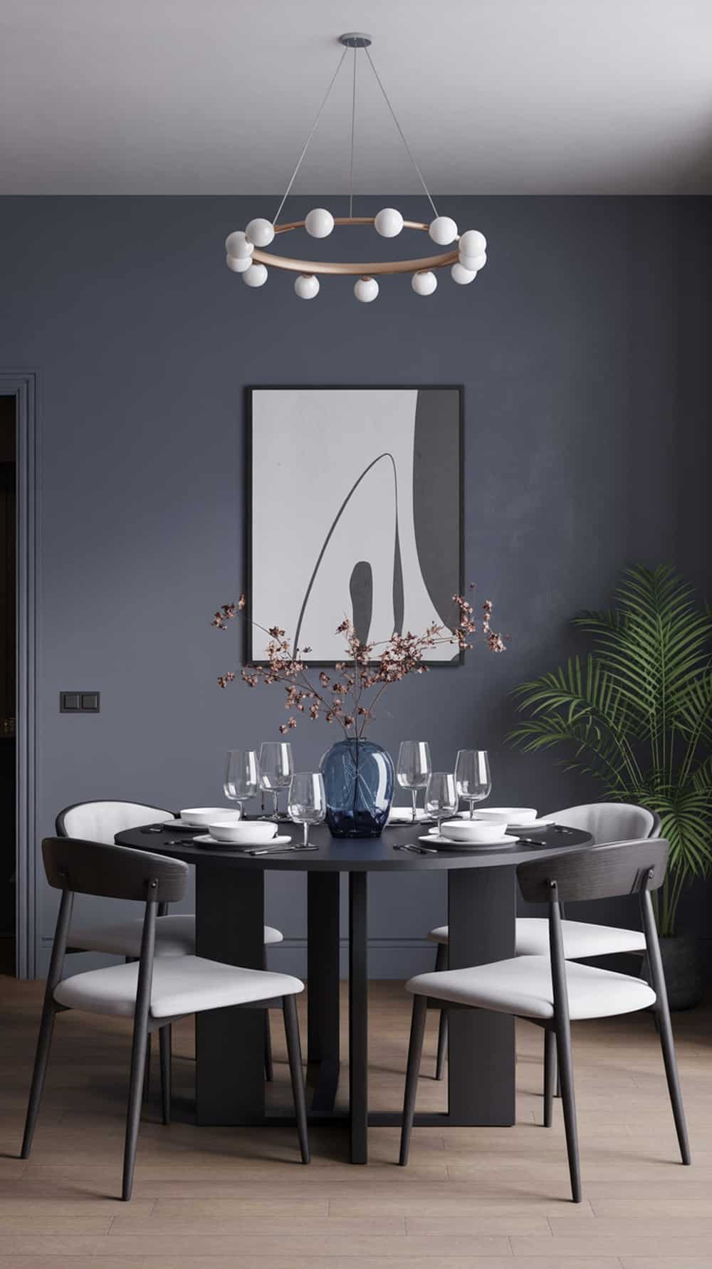 Dining room with slate blue accent wall, round table set with glassware, modern chandelier, and a potted plant.