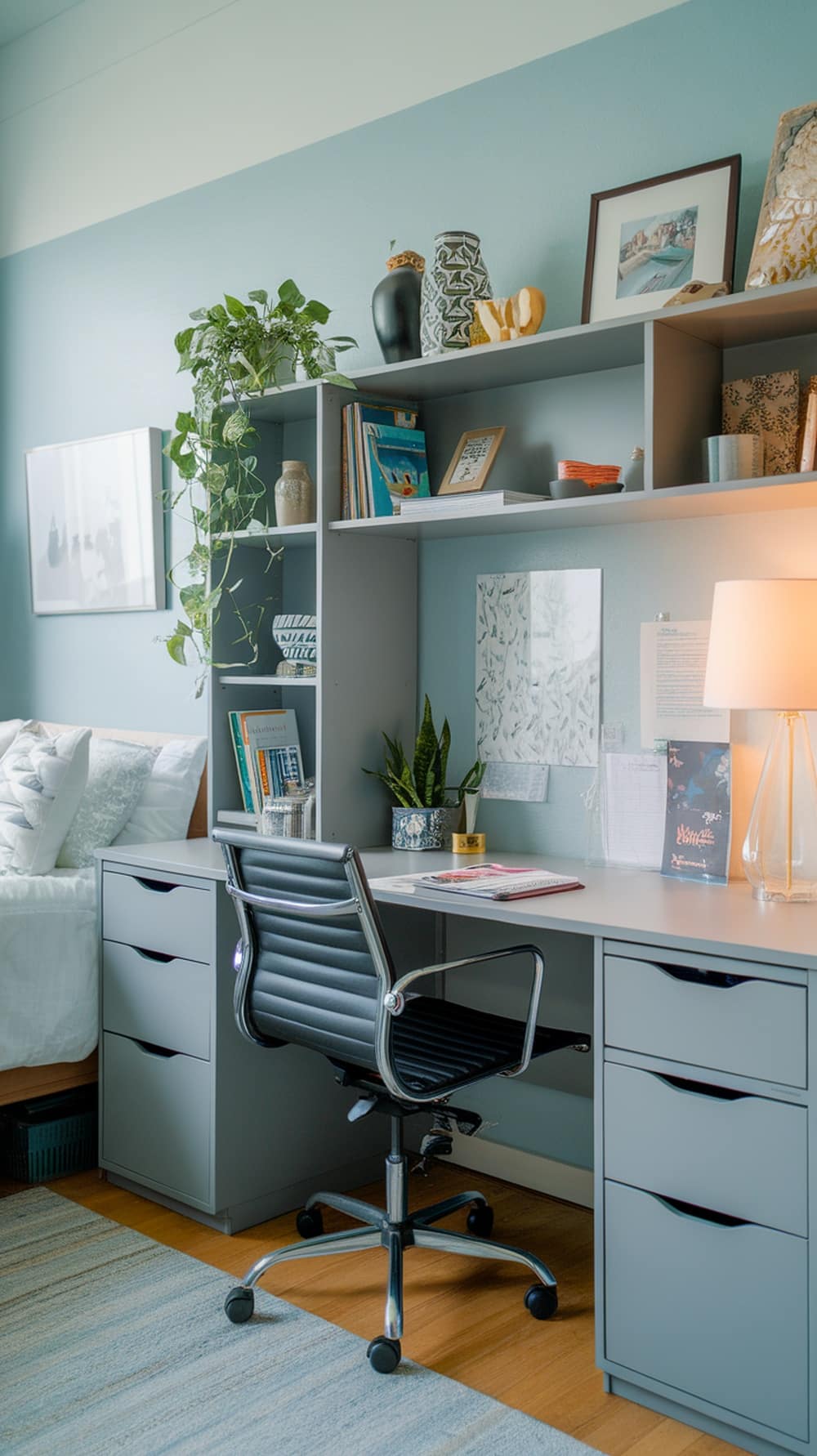 A cozy dorm room setup featuring gray furniture, a desk with a chair, and a shelving unit with decorative items.