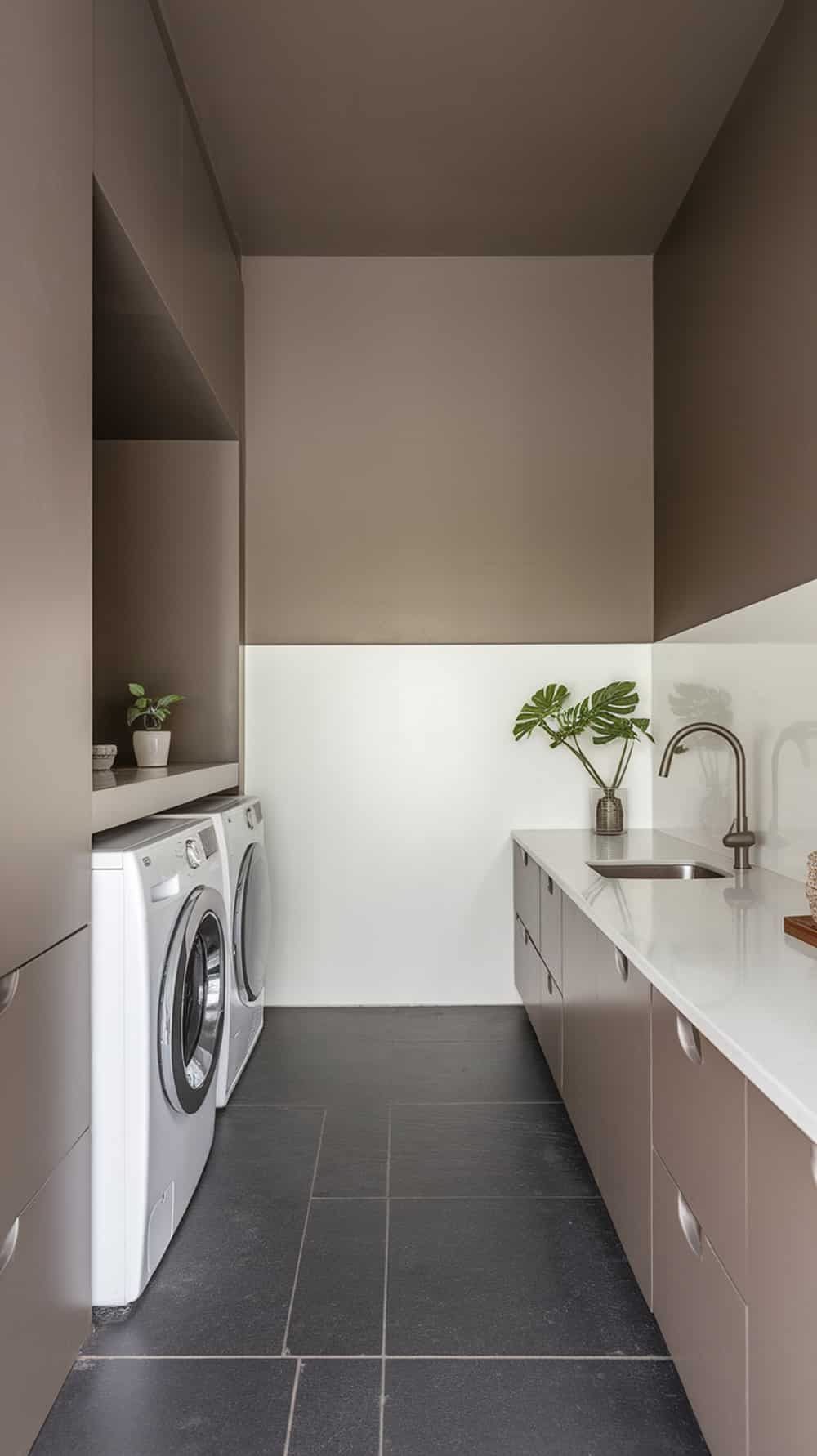 A minimalist laundry room featuring taupe cabinets, white walls, and dark flooring.