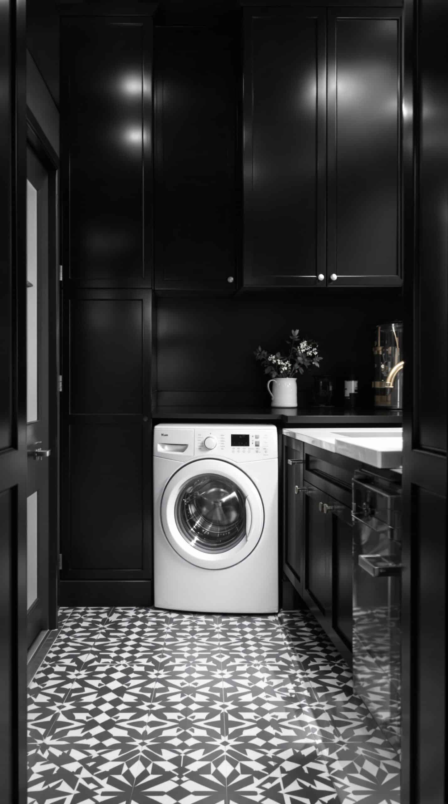A modern laundry room featuring black cabinetry and a geometric monochrome tile floor.