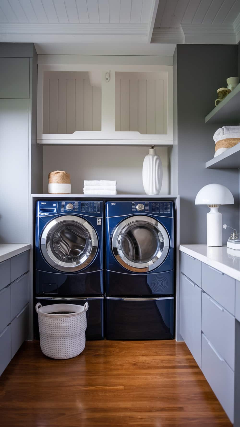 A navy blue washer and dryer pair in a stylish laundry room with gray cabinetry and wooden flooring.