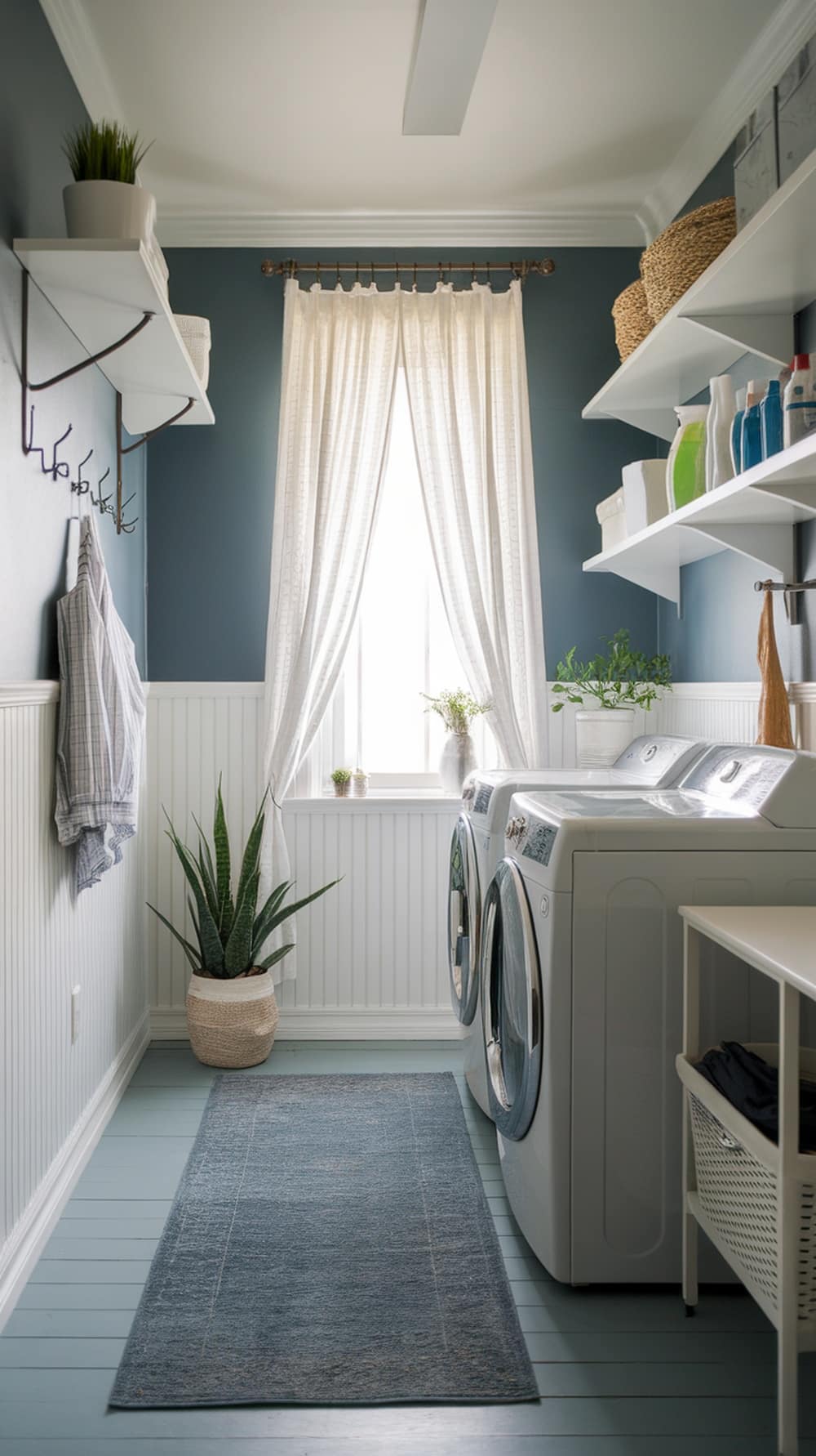 A modern laundry room featuring slate blue walls and white accents, with natural light and plants.
