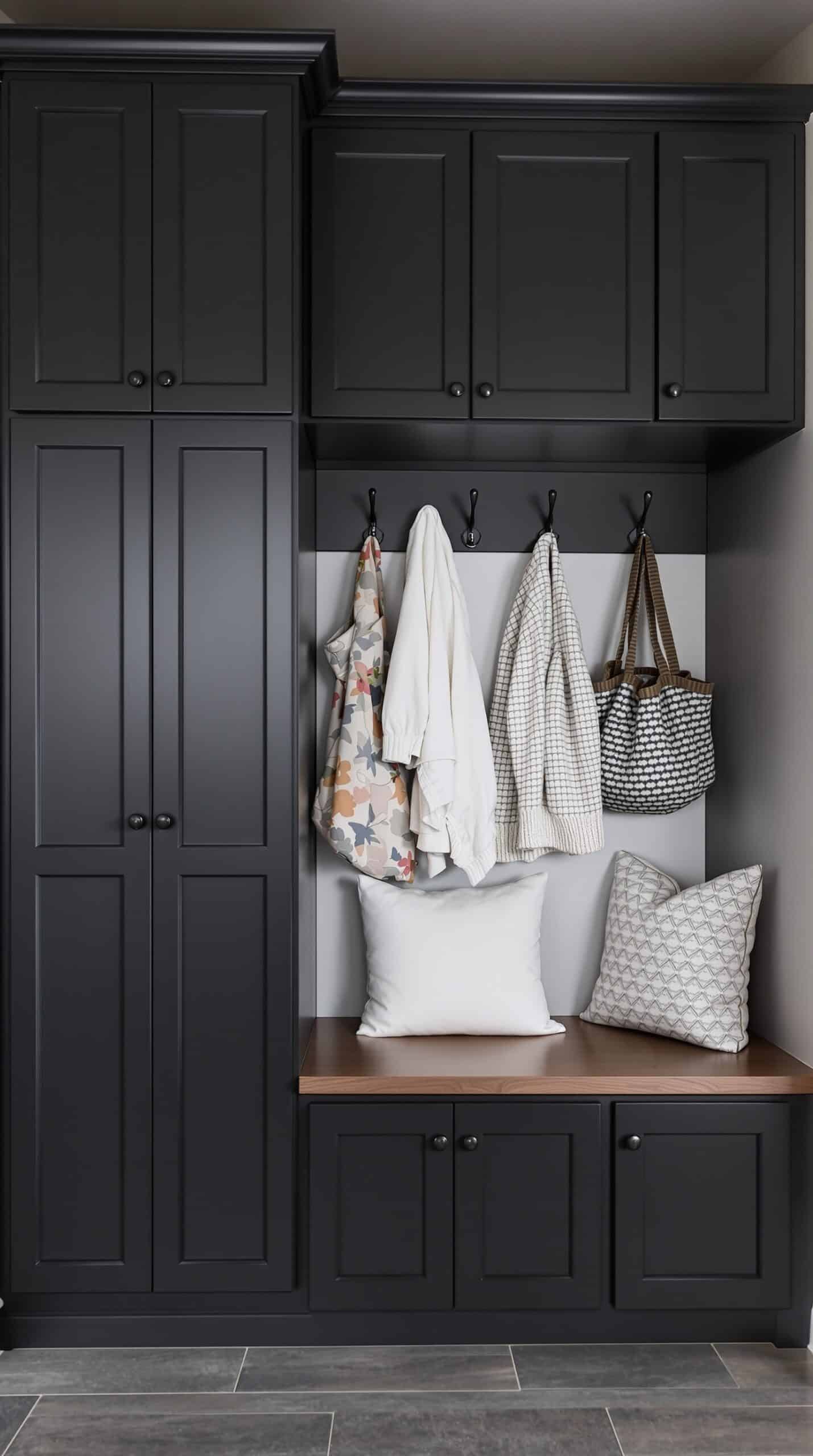 A modern mudroom-laundry combo featuring black cabinetry, hooks for hanging items, and a wooden bench.