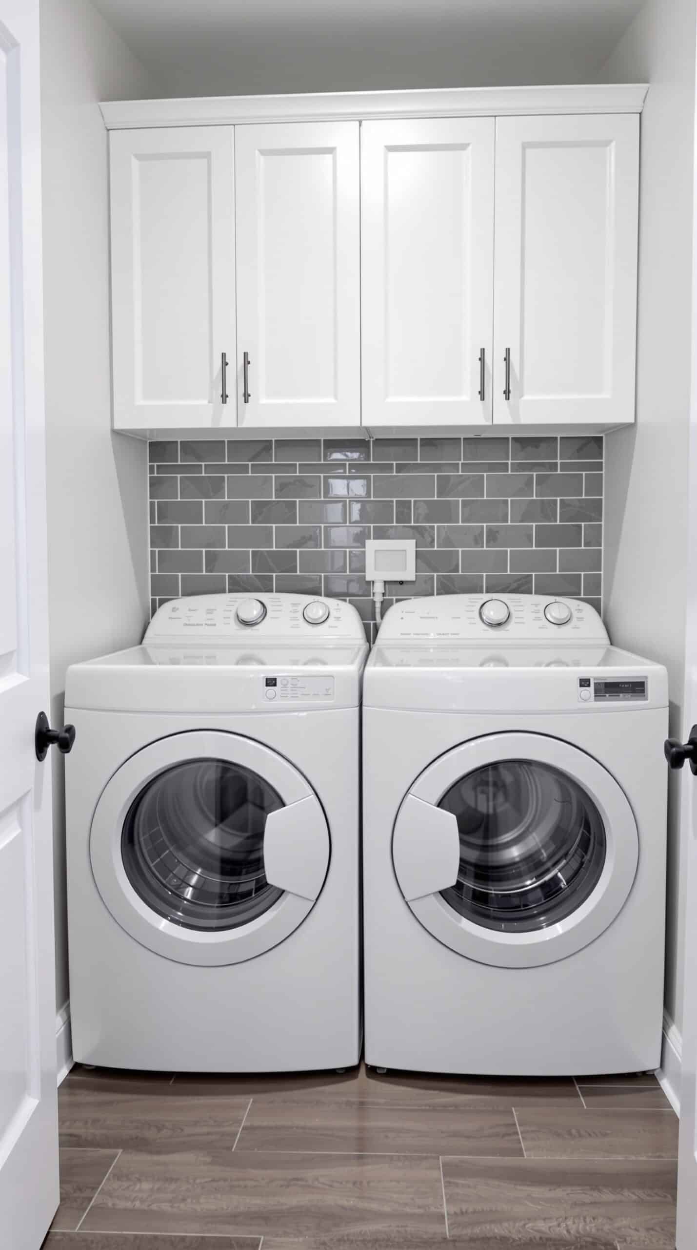 Laundry room with gray subway tile backsplash, white cabinets, and modern appliances.